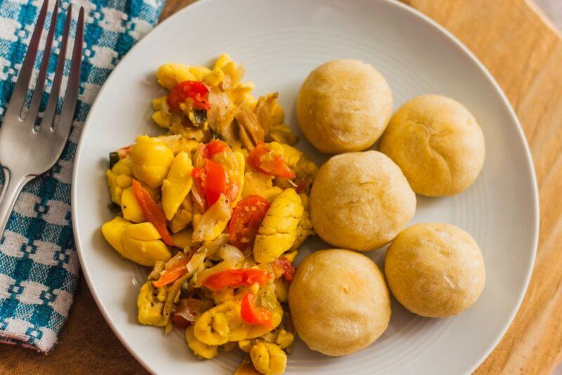 A white plate with fresh dumplings, cod, and ackee