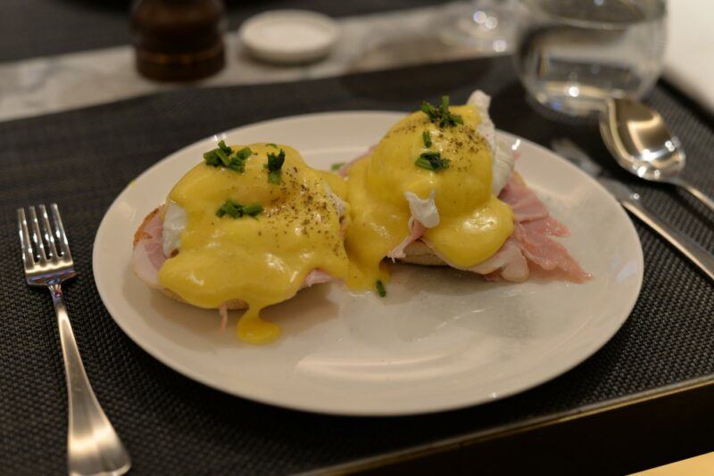 A white dish with two servings of eggs benedict and some cutlery