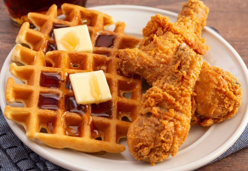 A white plate with two waffles, maple syrup, and butter, plus fried chicken