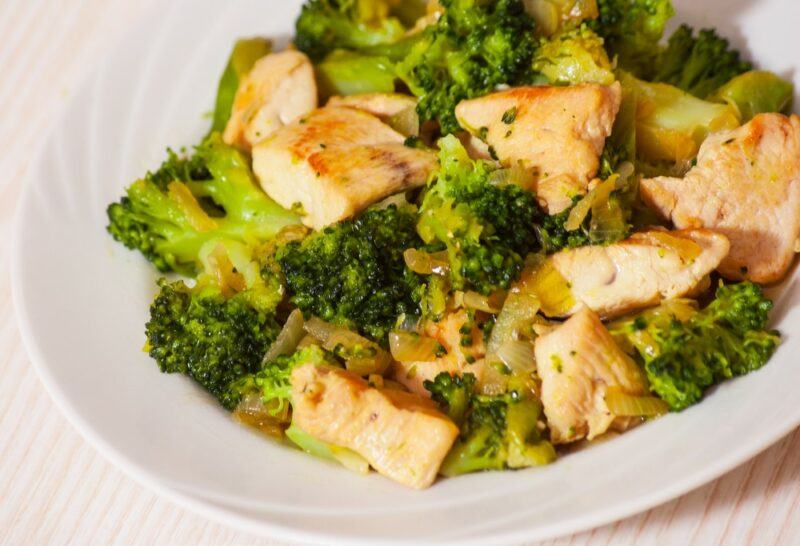 A white plate containing garlic chicken and broccoli