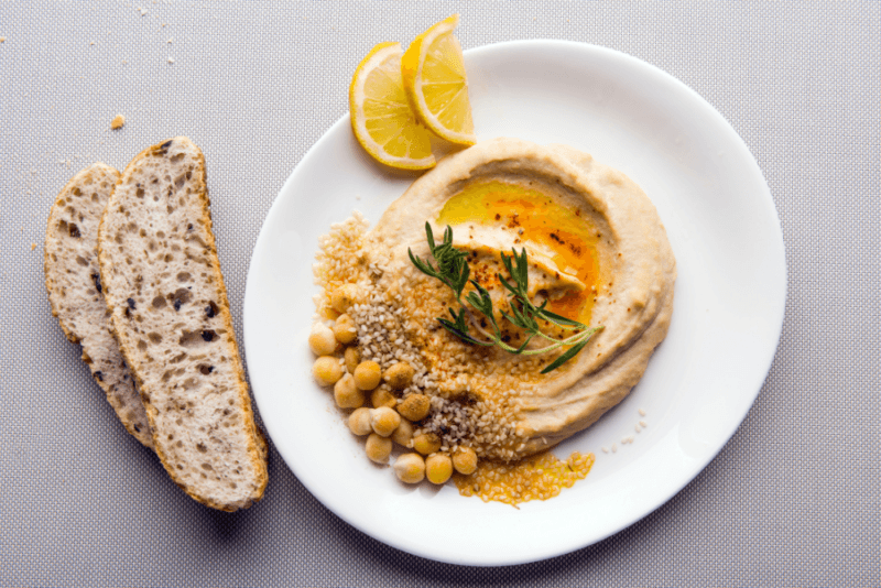 A large white plate with hummus, chickpeas, and two sliced lemons