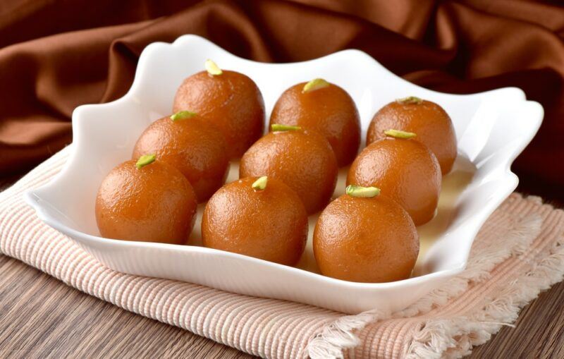 A white scalloped dish with nine pieces of gulab jamun dessert