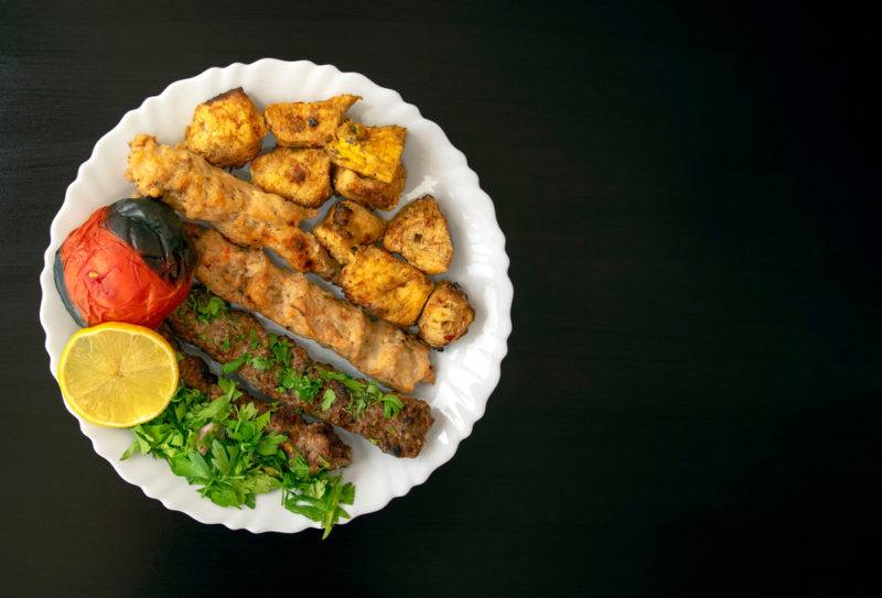 A white plate with Egyptian kofta and kebabs, along with some salads