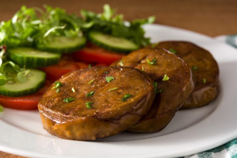 A white plate with tomatoes and cucumber, along with marinated and sliced seitan