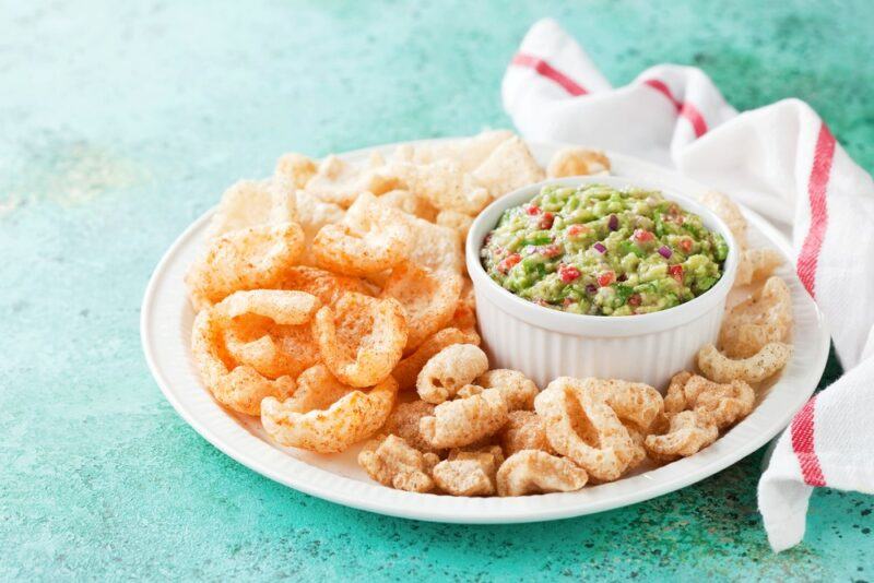 A large white plate of pork rinds, of two types, with a white bowl containing dip