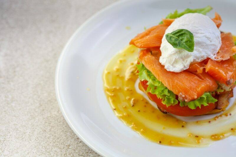 A white plate with salmon eggs benedict on a light colored table