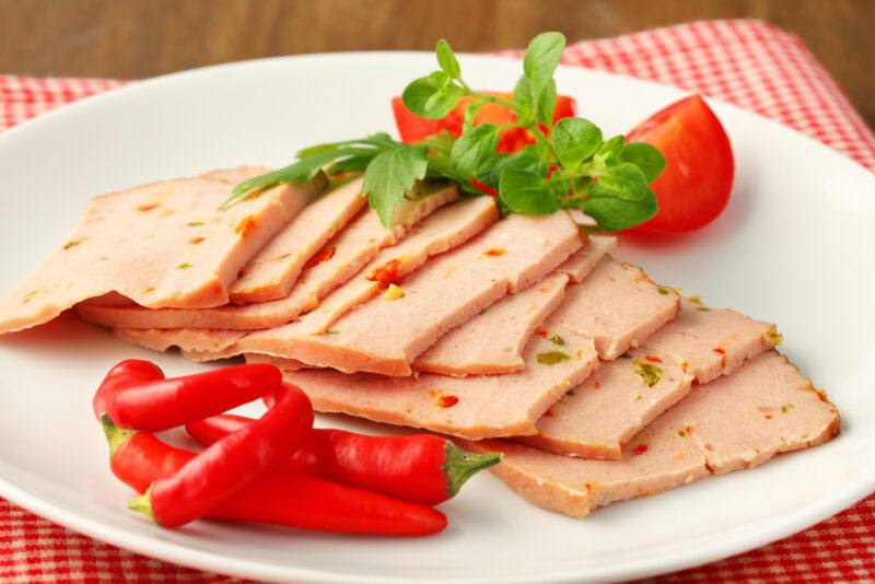 A white plate with thin slices of meatloaf, pieces of tomato, and peppers