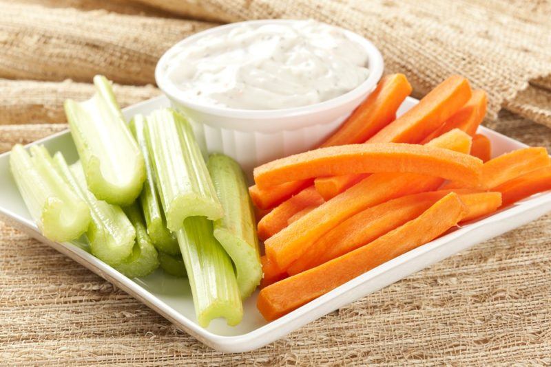 A white dish with dip, celery sticks, and carrot sticks