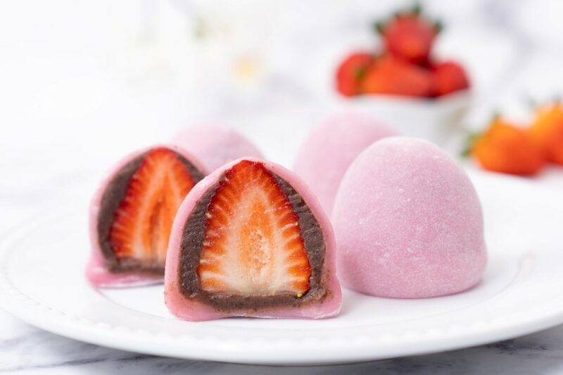 A white plate with strawberry mochis that include a whole strawberry and red bean paste inside