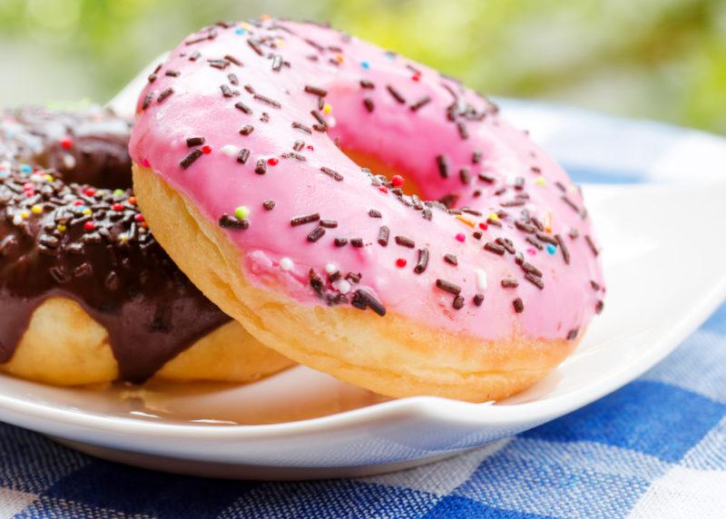 A white plate with a chocolate iced donut and a strawberry donut