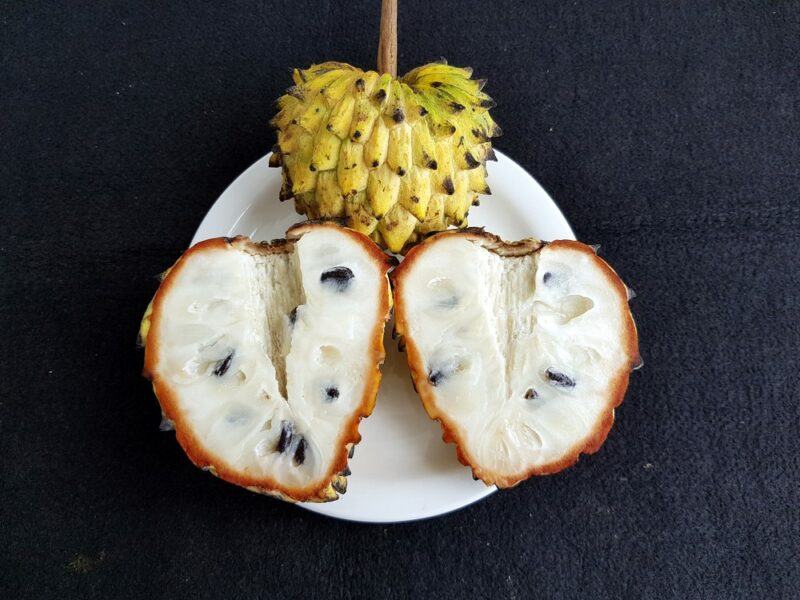 A white plate with a single yellow skinned custard apple and two pieces of the fruit that have been cut in half