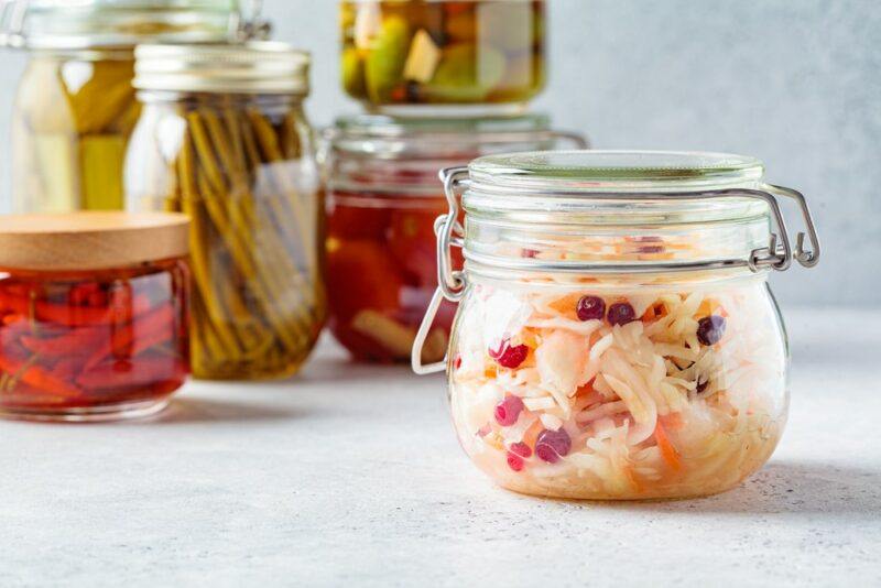 A white table with various jars of fermented food in the background, plus a jar of fermented cabbage and berries in the foreground.