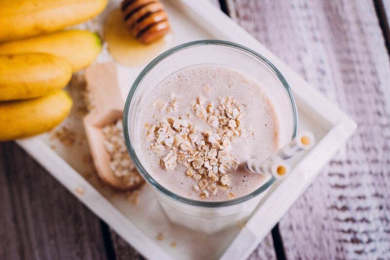 A white tray with bananas, oats, honey, and a wooden scoop