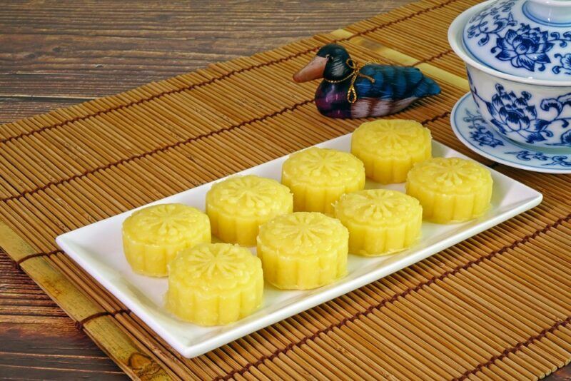 A white rectangular tray with yellow mung bean cakes, next to a duck and a blue and white piece of pottery