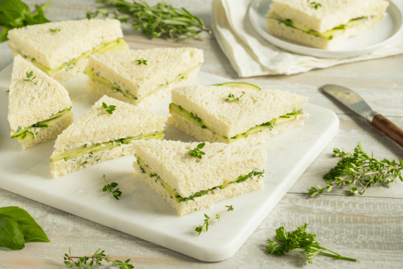 A large white tray with triangular cucumber tea sandwiches. They look like they're ready to serve at a party.