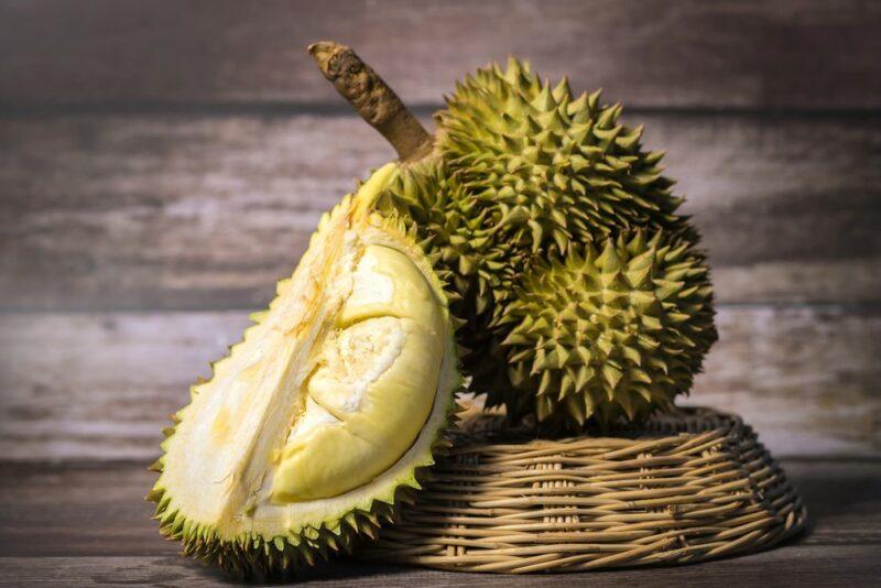 A whole durian fruit on an upturned brown woven bowl, plus half a durian fruit leaning against it