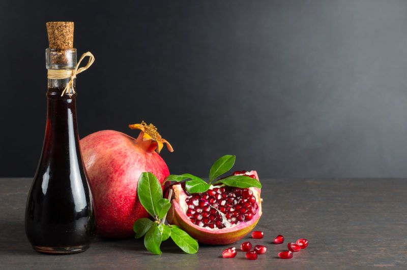 A full pomegranate, a pomegranate section, and a bottle of pomegranate juice on a black table against a black background