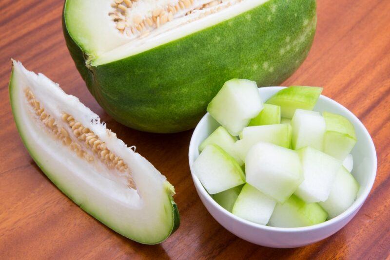 A large winter melon, next to a wedge of the fruit and some cut up pieces