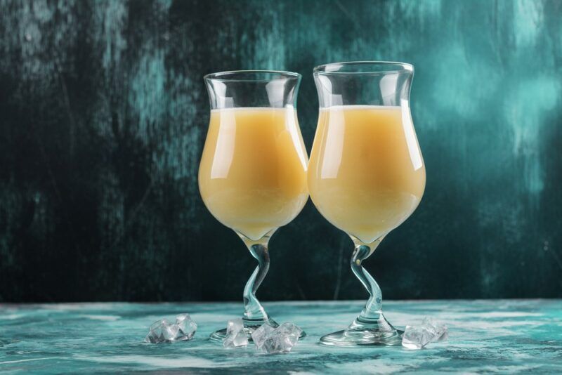 Two tall glasses containing a winter sunshine rum cocktail against a blue background