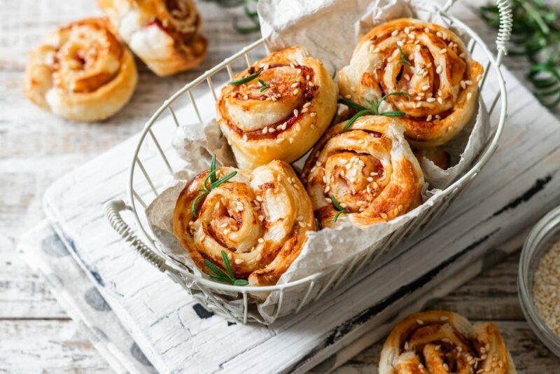 A basket containing handmade pizza scrolls, with more pizza scrolls off in the background