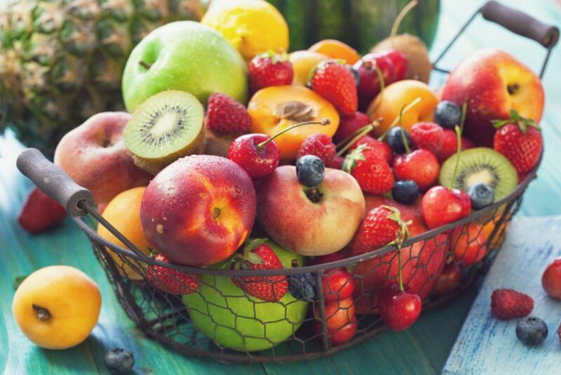 A wire basket with a variety of fresh fruits, including kiwis, peaches, and apples