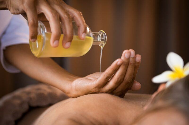 Someone pouring massage oil onto their hands, about to give a woman a massage