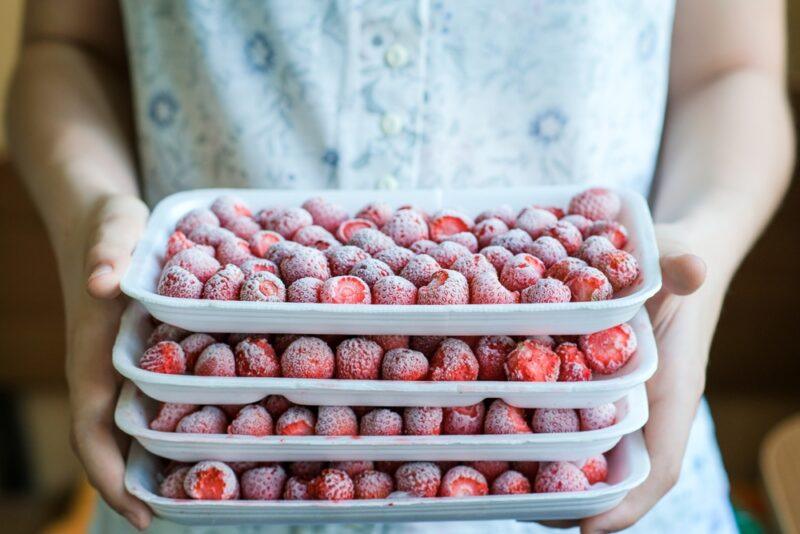 A woman holding three trays of frozen strawberries