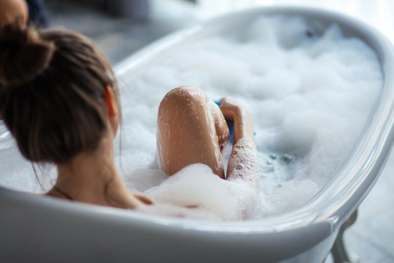 A young woman taking a bath that it filled with bubbles