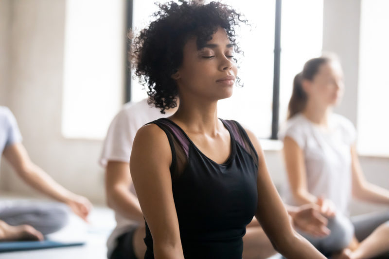 A woman in a meditation class working to decrease stress with other women in the background