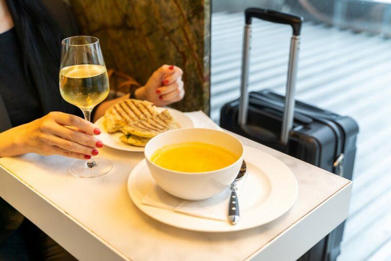 A woman sitting at a table in the airport with food, a glass of wine, and a bowl of soup