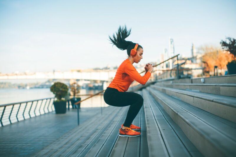 A woman outside wearing an orange shirt jumping on stairs as a form of cardio exercise