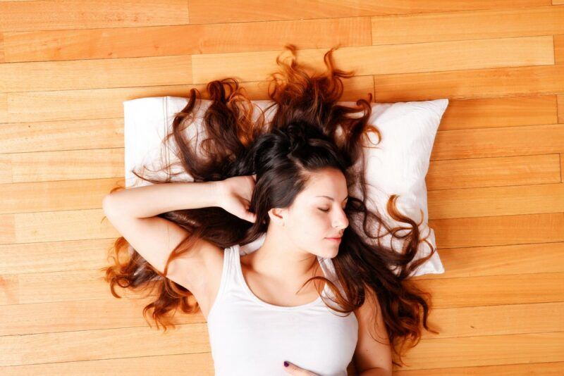 A young woman on a wooden floor with her hair splayed out across a pillow