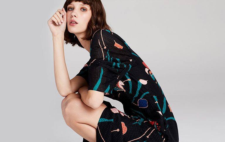 A brown haired woman crouching wearing a black and colored dress from Rebecca Taylor RNTD