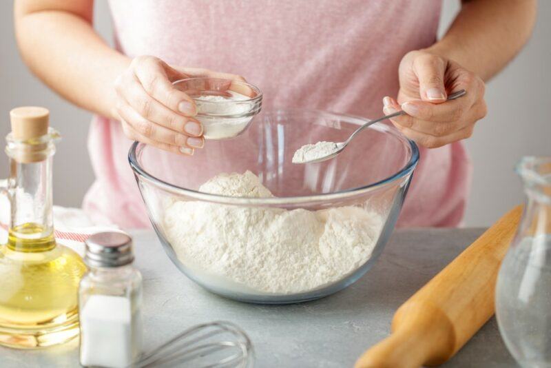 A woman baking in a glass bowl, measuring ingredients that include baking powder