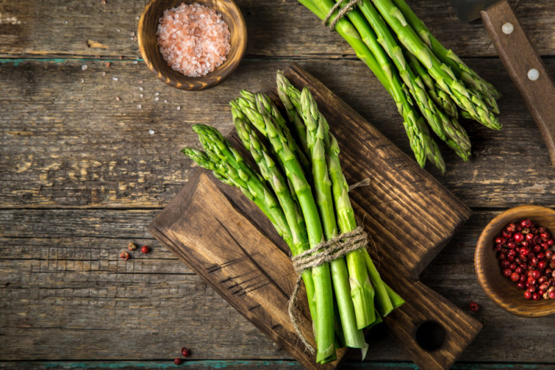 A wooden board with a bundle of asparagus, next to another bundle