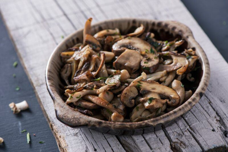 A brown bowl containing cooked mushrooms on a wooden board