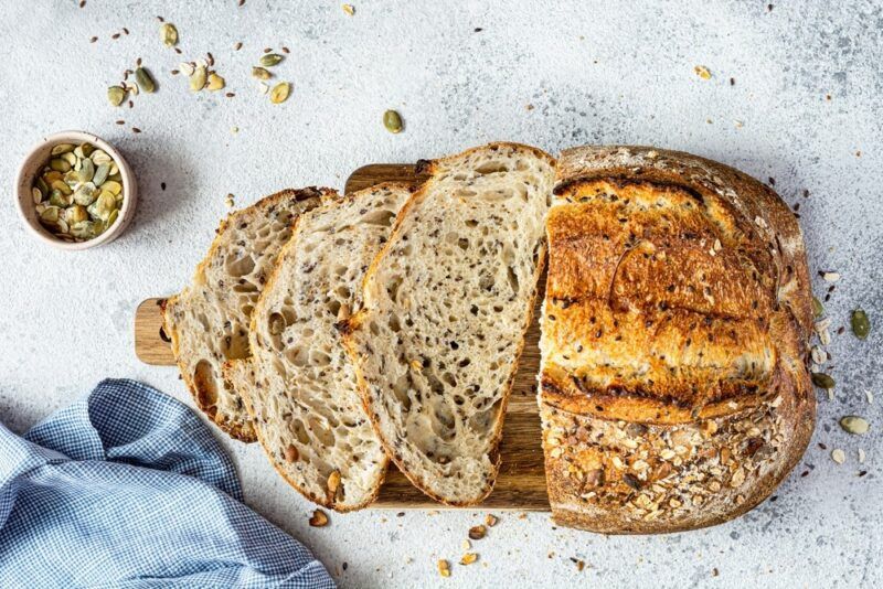 A loaf of seed and oatmeal sourdough on a table with a few slices