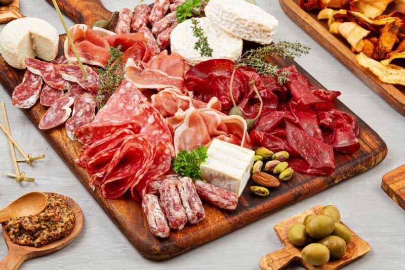 A wooden board containing a selection of cold cut meat, plus cheeses and olives