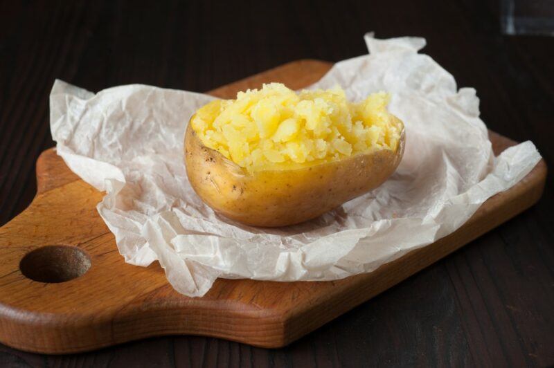 A wooden board with a piece of paper and a single baked potato