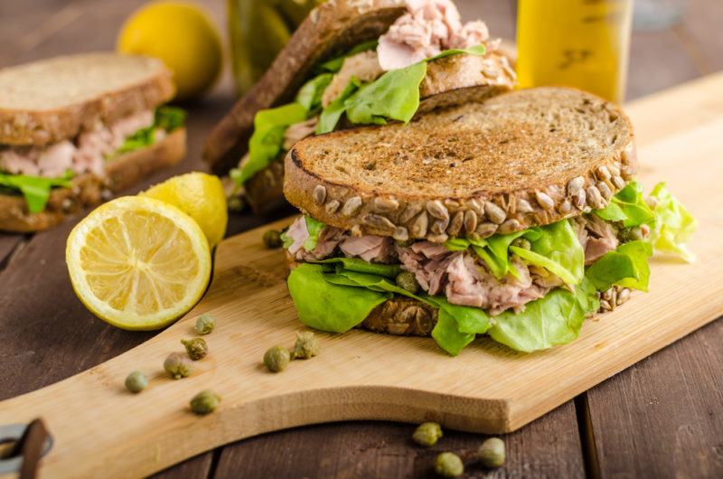 A wooden board with a tuna salad sandwich and a few in the background