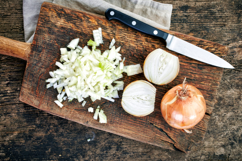 A wooden board with a whole onion, an onion chopped in half and diced onion