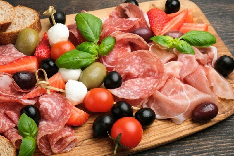 A large wooden board with antipasto ingredients, including olives, cheese, and tomatoes