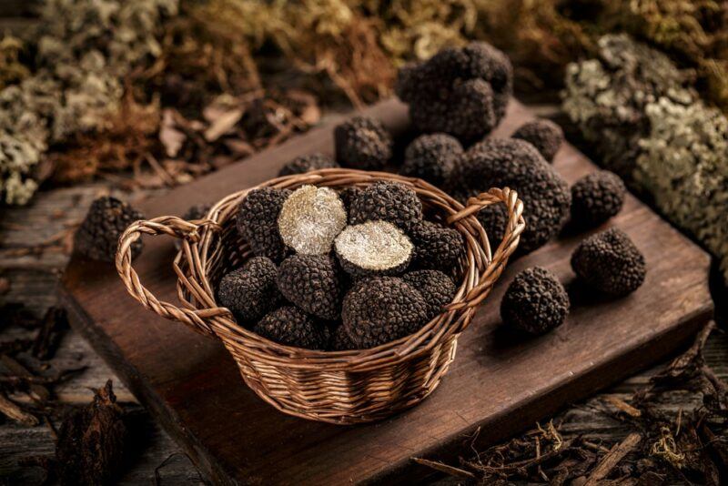 A wooden board with black truffles, next to a basket of more black truffles