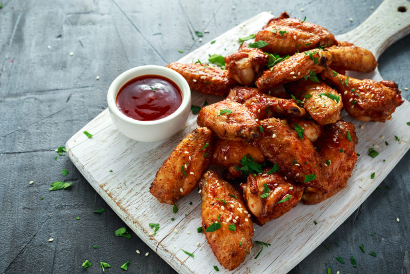 A wooden board with chicken wings and a tomato-based dip