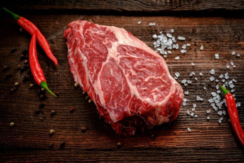 A wooden table with a chuck eye steak, salt, and chilis