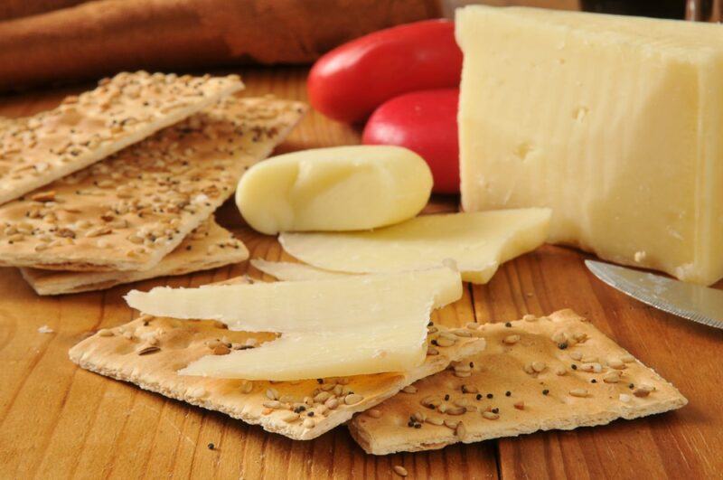 A wooden board with a selection of crackers and pieces of cheese