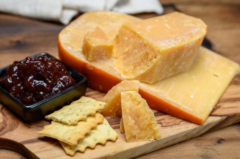 A wooden board with crackers, chutney, and plenty of cheese