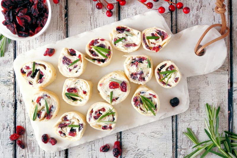 A white plate with cream cheese and cranberry pinwheels, with seasonal garnishes scattered around