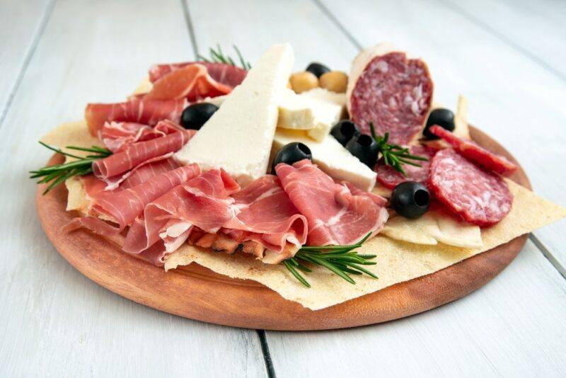 A wooden board with a collection of cured meat and cheese