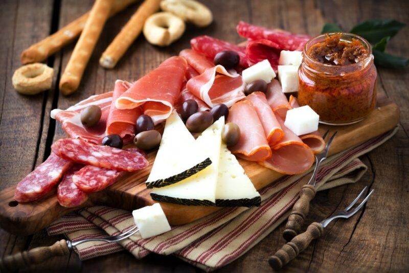 A wooden board with cured meat, cheese, crackers, chutney, and olives